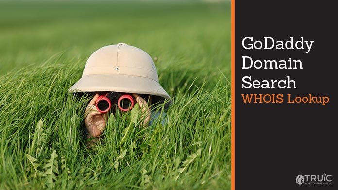 Person in a safari hat looking through tall grass with binoculars.