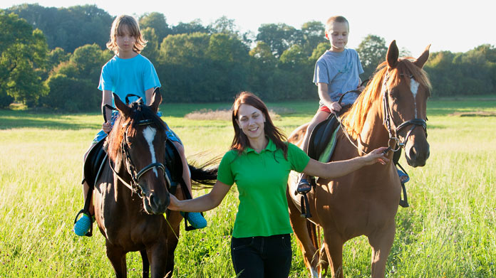 Two children on horses being guided by an instructor