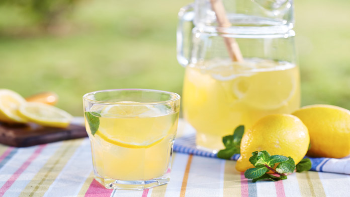 A glass of lemonade next to a pitcher and lemons