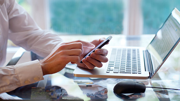 A person using their phone in front of a laptop