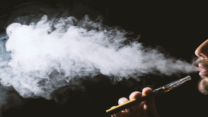 person holding and smoking a vape pen creating a vape cloud